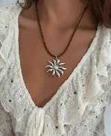 Collar con cordón trenzado color marrón y dije colgante de acero quirúrgico hipoalergénico con forma de flor o sol estilizado, con centro de piedras brillantes.