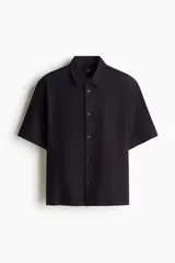 Camisa negra de manga corta en mezcla de lino y viscosa, con cuello inglés, tapeta lisa, canesú en la espalda y bajo recto. Corte holgado.