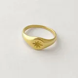 Anillo de acero dorado con diseño de estrella grabada, de forma elegante y minimalista.