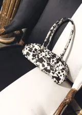 Cartera baguette de cuero con estampado de manchas de vaca en blanco y negro, con asa corta y cierre metálico.