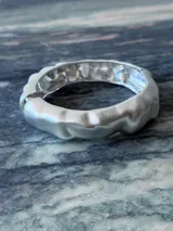 Pulsera rígida plateada con forma irregular y terminación mate.