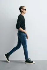 Pantalón de jean azul oscuro con efecto lavado y roturas en las rodillas, de corte ajustado al cuerpo desde la cintura hasta el tobillo.