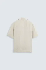 Camisa color marrón oscuro de corte relaxed fit, confeccionada en tejido de lino. Tiene cuello bowling, manga corta, bajo con aberturas laterales y cierre frontal de botonadura.
