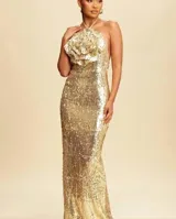 Vestido largo de fiesta color dorado con lentejuelas y diseño ajustado. Presenta cuello halter con detalle de flor grande en el pecho.