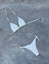 Conjunto de bikini color crema con corpiño triangular con detalle de estrella dorada y bombacha con tiras laterales.