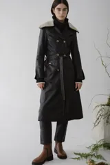 Trench de cuero color negro con cuello de piel sintética color crema, doble botonadura, cinturón y largo midi.