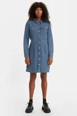 Vestido camisero de denim azul con calce amplio, cuello camisero, mangas largas con puños abotonados, cierre frontal con botones y bolsillos en el pecho.