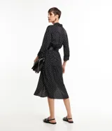 Vestido midi tipo chemise de tela satinada negra con lunares blancos, cuello solapa, abotonado delantero, mangas largas y cinturón con hebilla.