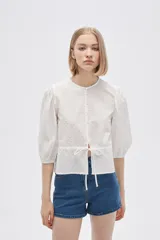 Blusa blanca de algodón con textura de lunares, corte recto, cuello redondo, mangas 3/4 abullonadas y cierre frontal con botones.