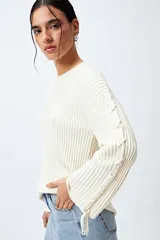 Sweater negro de punto canalé con detalle de trenzado en las mangas y lazo ajustable en el ruedo.