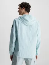 Campera con capucha Calvin Klein, confeccionada en nailon 100% reciclado color celeste. Tiene cierre de cremallera frontal, cuello alto, bolsillos delanteros con cremallera, puños y dobladillo elásticos, tirador de cremallera con la marca e insignia con el logo de Calvin Klein en la manga.
