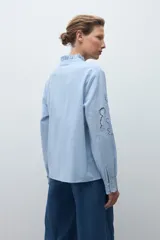 Camisa de algodón celeste claro, de manga larga, con cuello mao con volados y bordados calados florales en el frente y las mangas.