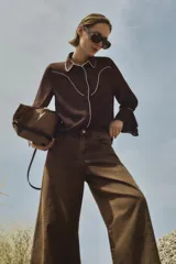 Camisa marrón de mangas largas con botones y detalles de pespuntes blancos en cuello, solapa y canesú.