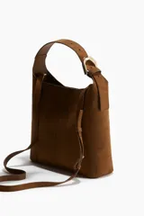 Cartera marrón de gamuza sintética con correa fina ajustable y asa ancha con hebilla metálica dorada.