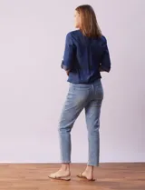 Blusa de tencel azul con cuello a la base y escote en V, abertura central con botones, bolsillos delanteros, mangas 3/4 regulables con presilla y botón, y terminación de ruedo con nudo.