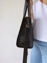 Cartera tipo tote bag de cuero color negro, con doble asa corta de mano y correa larga regulable y extraíble para usar al hombro o cruzada. Tiene un bolsillo frontal con cierre y un bolsillo interno.