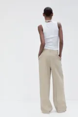 Pantalón color beige de tiro medio con trabillas, pliegues frontales y corte ancho.
