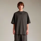 Camiseta de algodón color verde oscuro, corte oversize, con cuello redondo y un pequeño parche rectangular negro en el pecho.