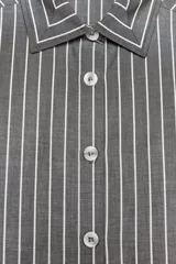 Camisa corta gris con rayas verticales blancas, cuello solapa y manga larga. Cierre frontal con botones.