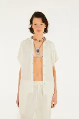 Camisa blanca de algodón con textura arrugada, corte holgado, mangas cortas, cuello clásico y cierre frontal con botones.