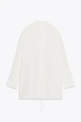 Camisa blanca a rayas verticales, de cuello redondo y manga larga con puños. Presenta cierre frontal con cordones ajustables con lazadas y abertura en la espalda ajustable con lazadas.