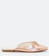 Zapatilla mule color rosa metalizado, con punta redonda, lazo decorativo en la parte superior, interior de piel sintética y suela plana.
