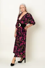 Vestido midi negro con estampado floral fucsia y marrón, escote en V cruzado, mangas largas y cinturón ancho negro con hebilla circular.