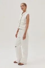 Chaleco de denim blanco con costuras en contraste color ocre, cuello camisero, cierre frontal con botones, bolsillos de parche con solapa en el pecho y sisas desflecadas.