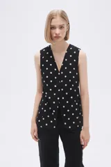 Chaleco largo sin mangas negro con estampado de lunares blancos, cuello en V y corte entallado.