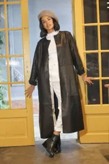 Tapado largo de cuero negro, de corte recto, sin botones ni bolsillos y cuello a la base.