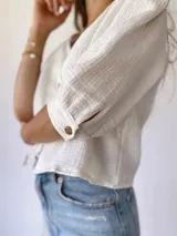 Blusa color crudo de muselina con botones de madera, manga tres cuartos y corte holgado.
