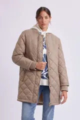 Campera larga acolchada color visón, con cuello redondo, cierre frontal con botones a presión y bolsillos laterales con cierre.