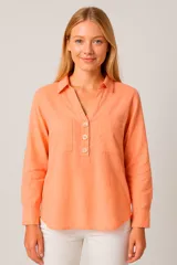 Blusa color salmón de manga larga con cuello camisero y escote en V con tres botones de madera. Tiene dos bolsillos de parche en el pecho.