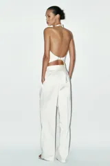 Pantalón blanco de tela satinada, tiro alto, corte ancho y pliegues en la parte delantera y trasera.
