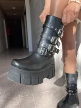 Bota negra de ecocuero con caña media, plataforma track y tres correas con hebillas plateadas.