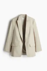 Blazer color beige de corte recto, con solapas de pico, bolsillos delanteros con solapa y mangas con forro a rayas.