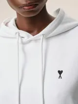 Buzo con capucha color verde oliva, con cordones ajustables y bolsillo tipo canguro. Logo bordado de corazón negro en el pecho. Corte holgado.