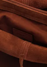 Bolso tipo shopper de gamuza color marrón, con doble asa corta y asa larga para el hombro. Tiene cierre de lazo y forro interior de algodón con un bolsillo con cremallera.