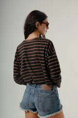 Camiseta de manga larga, corte holgado, con cuello redondo y estampado de rayas horizontales en tonos negro y marrón.