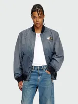 Campera bomber Diesel modelo J-Kepes, color gris azulado con efecto desgastado o tie-dye sutil. Presenta cuello, puños y cintura de punto elástico en color negro. Lleva un parche grande con el logo 'D' de Diesel en el pecho izquierdo.