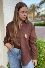 Camisa marrón de lino con cuello clásico, manga larga, cierre con botones y bolsillo en el pecho con bordado de las iniciales 'PC'.