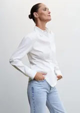 Camisa básica de algodón color blanca, con cuello camisero y manga larga, cierre de botones en la parte delantera.