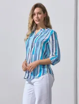 Blusa de gasa estampada con rayas verticales en tonos celeste, azul y blanco. Tiene cuello a la base con escote en V y abertura con botones. Las mangas largas son de largo regulable.