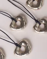 Collar con dije dorado irregular con agujero central, colgando de cordón negro ajustable.