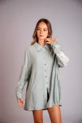Camisa celeste de corte clásico, con botones frontales y bordados florales en las mangas.