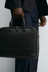 Maletín negro con acabado texturizado, compartimento principal con cierre de cremallera, bolsillo interior con cremallera, bolsillo frontal con cremallera, bolsillo trasero para dispositivos electrónicos de hasta 13 pulgadas y bolsillo trasero con cremallera. Tiene dos asas de mano y un asa de hombro ajustable y extraíble.