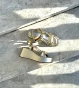 Sandalias doradas con plataforma, tiras cruzadas y hebilla al tobillo.