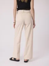 Pantalón de vestir color beige, de corte recto, con bolsillos laterales y traseros. Se ajusta a la cintura con cinturón de cuero marrón.