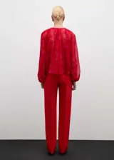 Blusa roja con estampado floral, de tejido fluido semitransparente y manga larga con puños elásticos. Tiene cuello redondo con cierre de lazo.