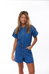 Mono corto de jean azul con cuello camisero, cierre frontal con botones, mangas cortas con dobladillo y bolsillos delanteros y traseros.